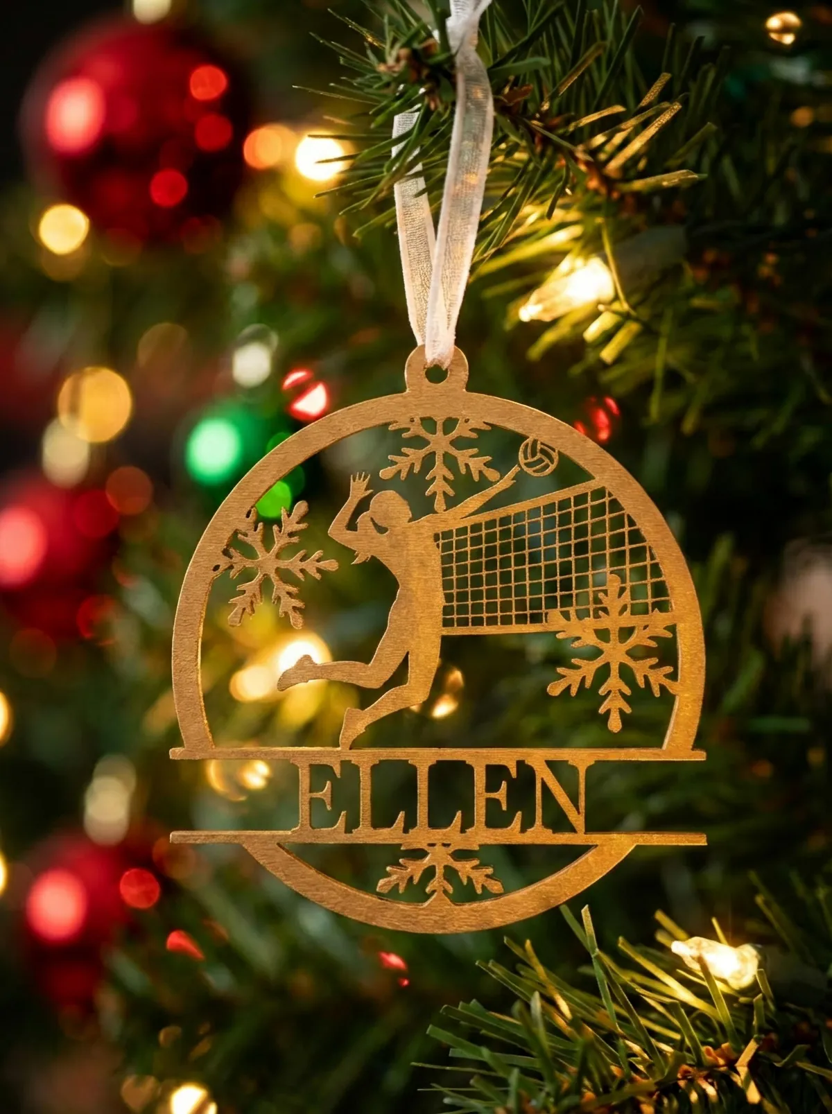 A laser-cut wood volleyball ornament with a detailed net and the name ELLEN, hanging on a lit Christmas tree